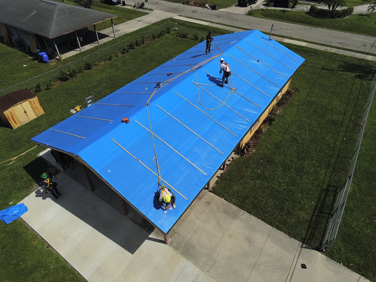 Workers applying a temporay blue roof to a building to protect it from hurricane damage