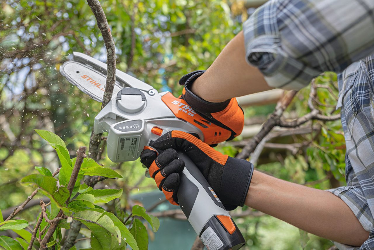 Close up of person wearing a plaid shirt and gloves trimming a branch from a tree.