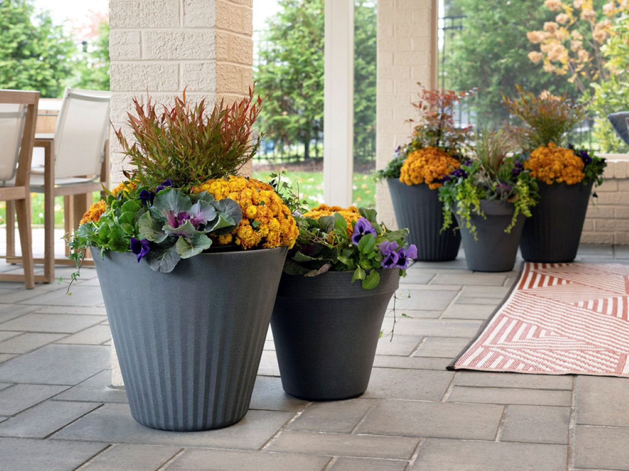 An arrangement of five planted pots with various colors and textures of flora on a lovely stone patio.